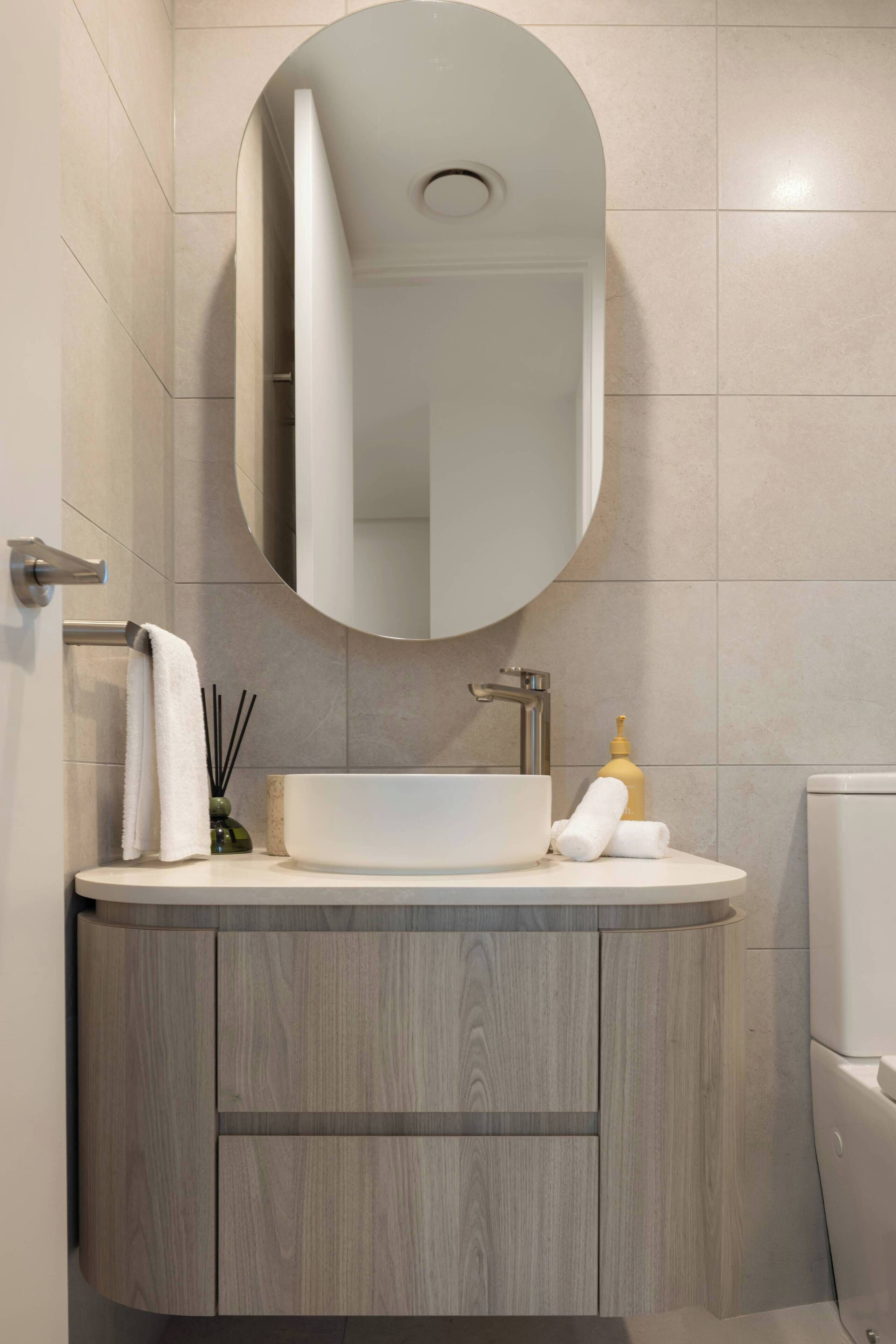 A bathroom with a round mirror, a white sink, and a toilet.
