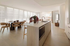 A modern kitchen with a central island, dining area with chairs, and a large window with sheer curtains. - Mahlo by Khove (Burleigh Heads)
