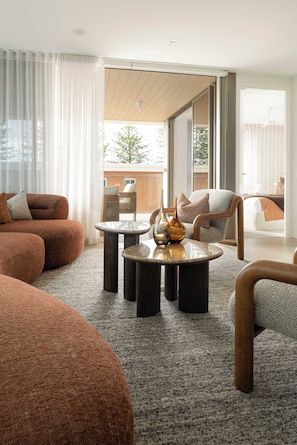 A modern living room with a sofa, armchairs, a coffee table, and a view through a sliding glass door to an outdoor area. - Mahlo by Khove (Burleigh Heads)