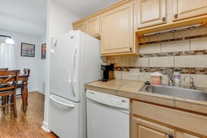 Eine Küche mit einem weißen Kühlschrank, einer Kaffeemaschine, einem Geschirrspüler und Holzschränken.
