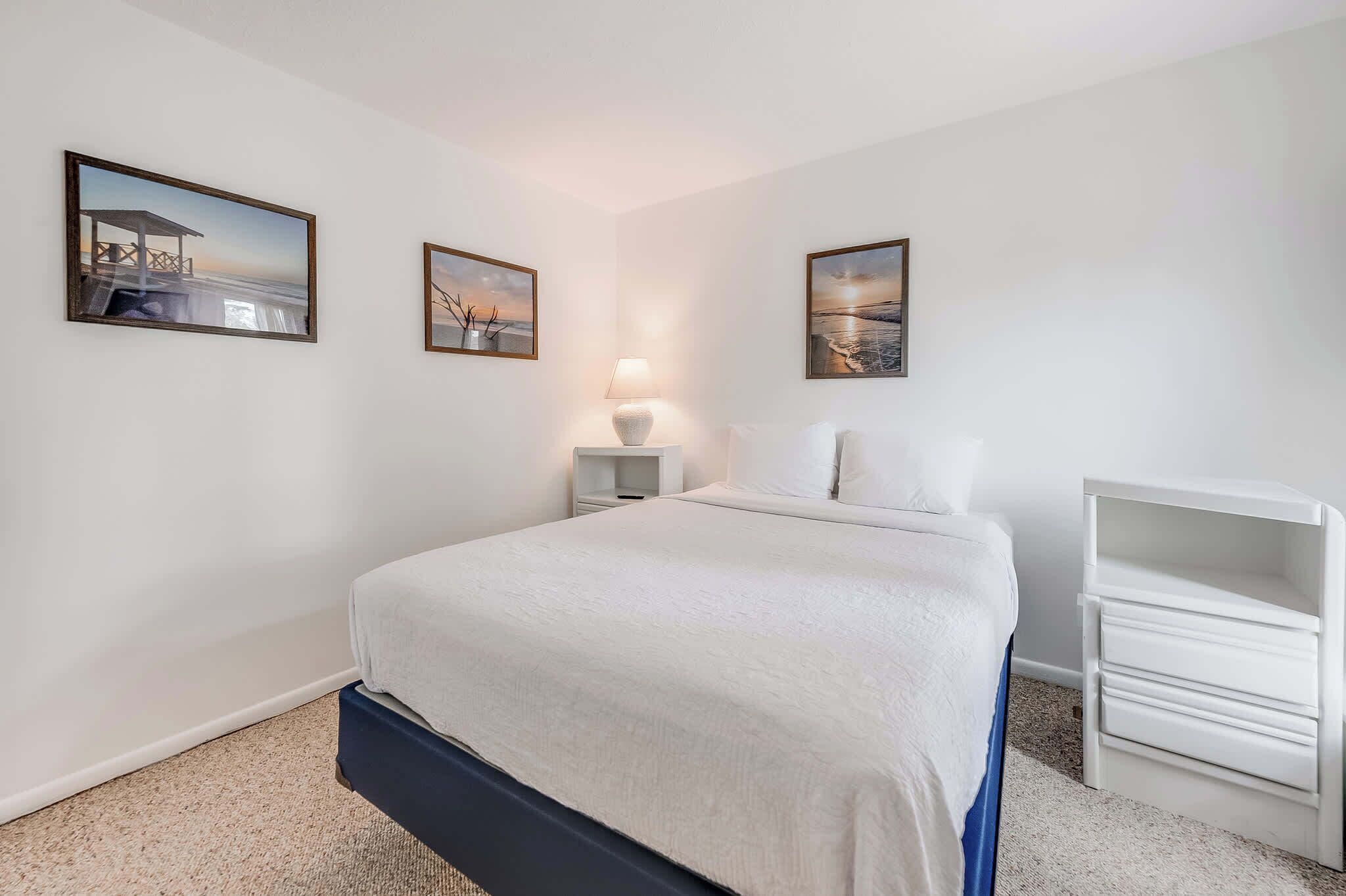 A bedroom with a bed, a nightstand, a lamp, and two framed pictures on the wall.