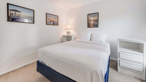 Een slaapkamer met een bed, een nachtkastje, een lamp en twee afbeeldingen in een lijst aan de muur.
