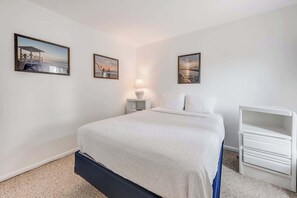 Ein Schlafzimmer mit einem Bett, einem Nachttisch, einer Lampe und zwei gerahmten Bildern an der Wand.