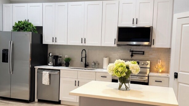 Una cocina moderna con armarios blancos, electrodomésticos de acero inoxidable y una isla central con taburetes.