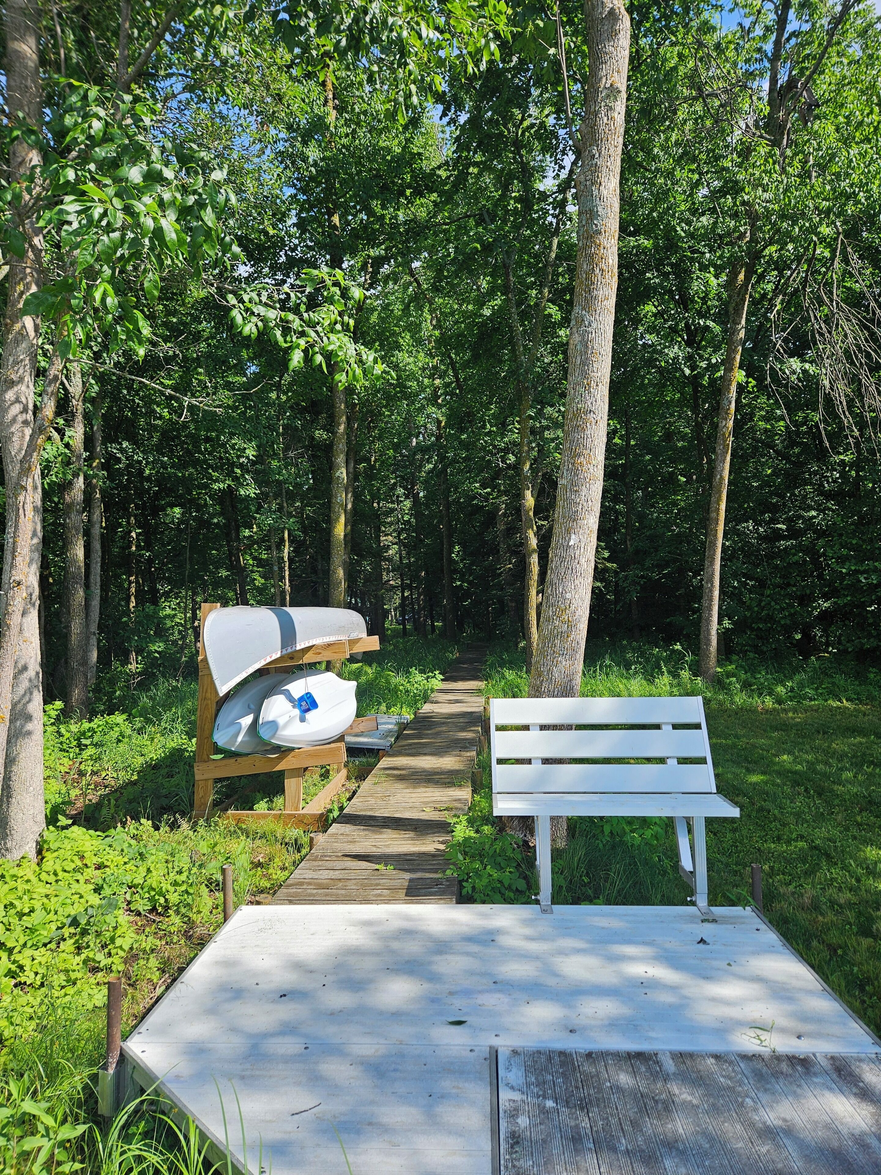 Un banc en bois et une table de pique-nique se trouvent dans une zone boisée, à proximité d’un sentier bien dégagé.