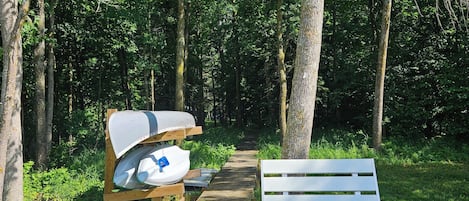 Un banc en bois et une table de pique-nique se trouvent dans une zone boisée, à proximité d’un sentier bien dégagé.