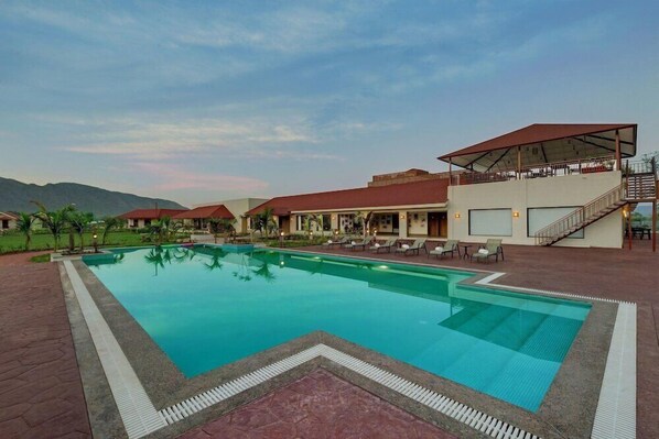 A hotel with a swimming pool, outdoor seating, and a covered area with stairs. - The Fern Sattva Resort Polo Forest (Vijayanagar)