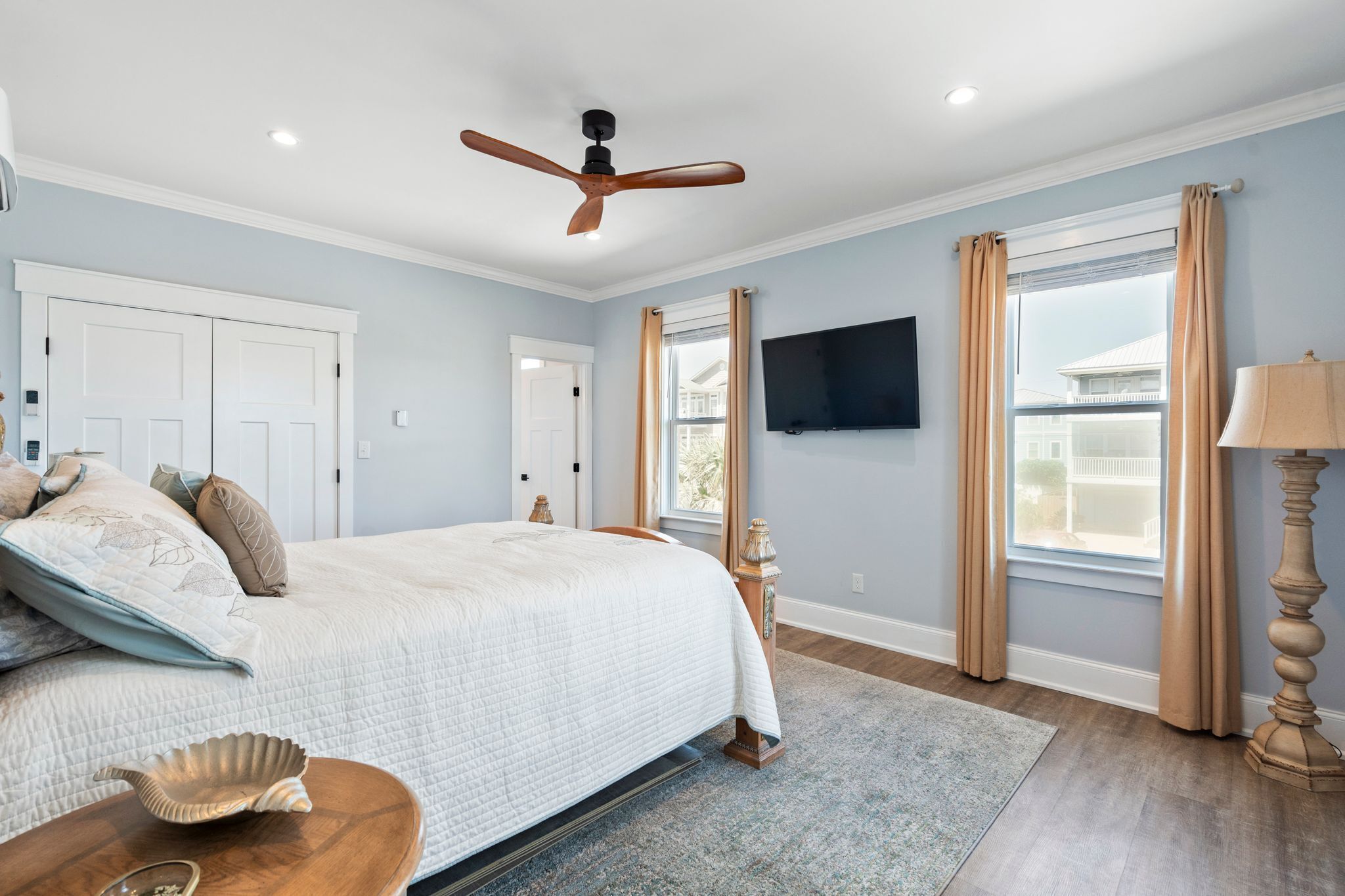A bedroom with a bed, a ceiling fan, a TV, and a window with curtains.