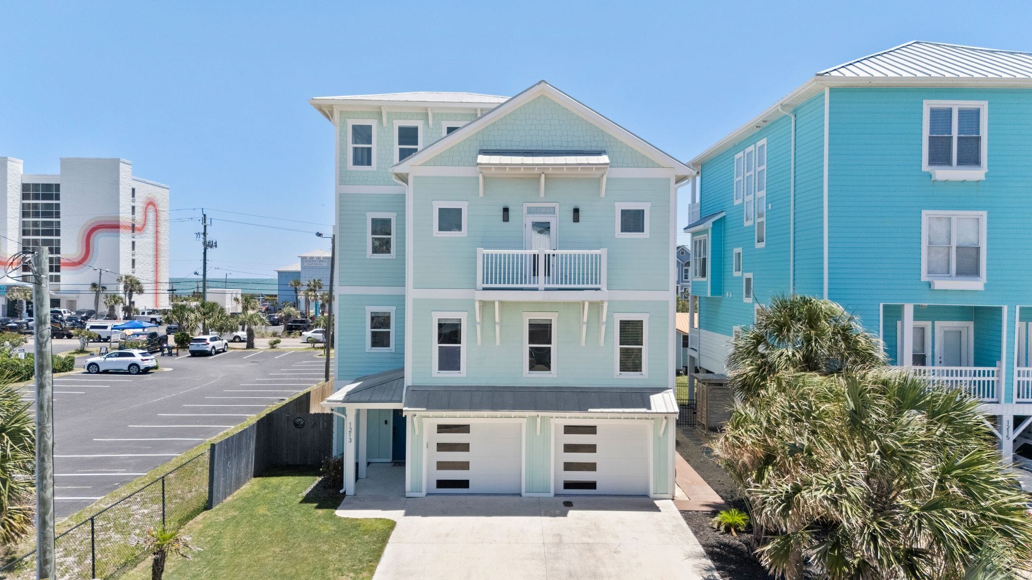 A multi-story residential building with a central balcony, a garage, and a parking lot in the foreground.