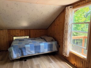 Ein Schlafzimmer mit Holzboden, einem Fenster mit Blick auf Grünflächen und einem Bett mit gemustertem Überwurf.
