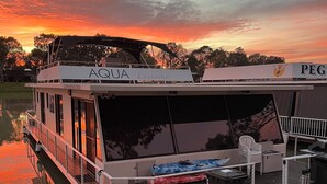 A leisure boat named AQUA with a covered deck area, a small seating area, and a trash bin. - 3-bedroom house boat in beautiful Swan Reach with beautiful Murray River views. (Punyelroo)