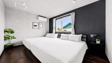 A modern bedroom with a large bed, a potted plant, and a view of a house through a window.