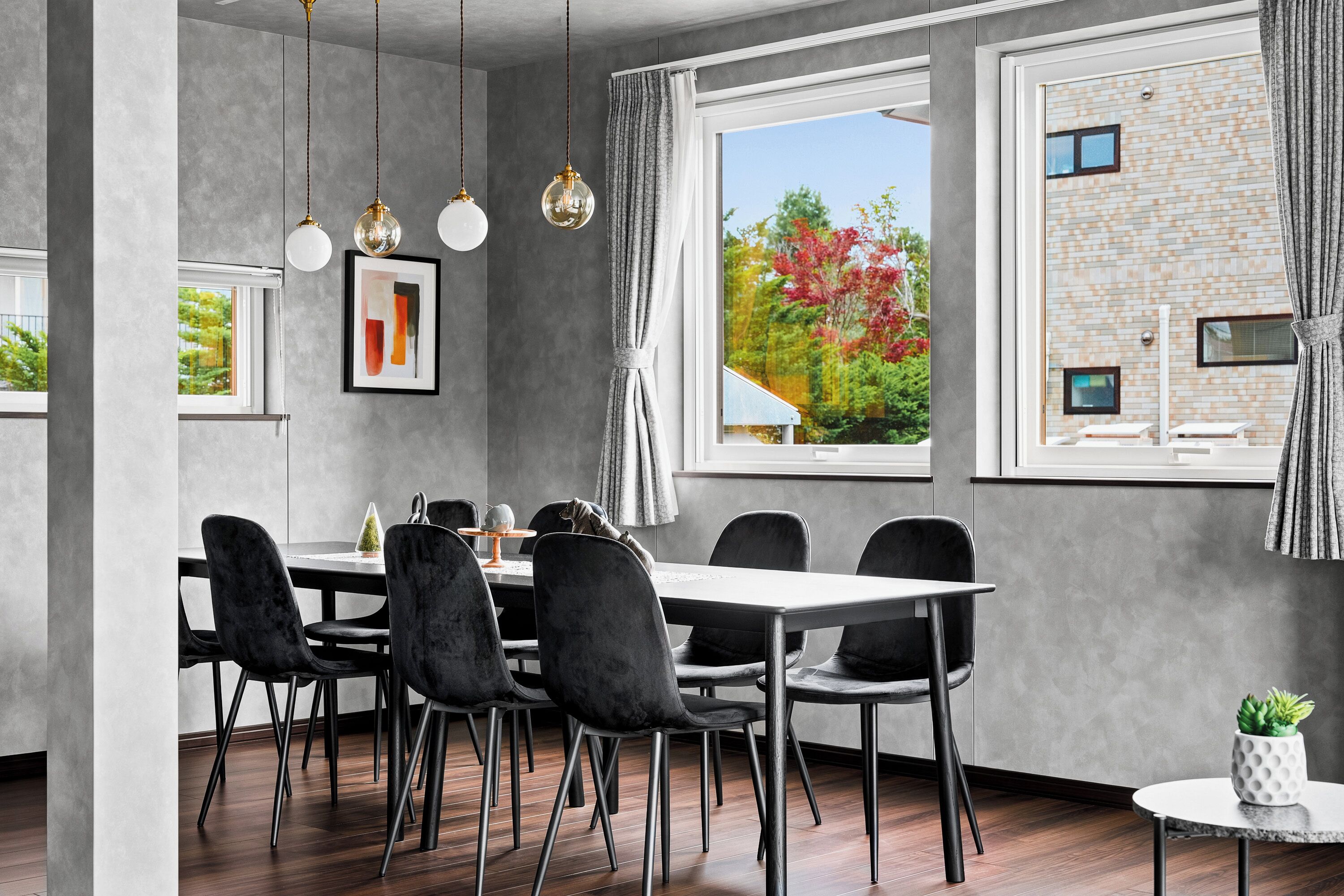 A modern dining area with a large table, six chairs, pendant lights, and a view of a brick building outside.