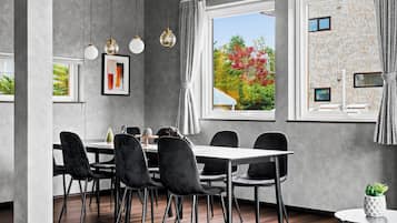 A modern dining area with a large table, six chairs, pendant lights, and a view of a brick building outside.