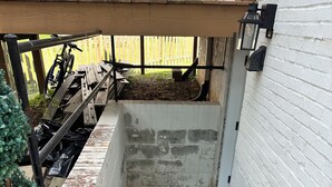 Una escalera de concreto lleva a una terraza de madera donde se encuentra estacionada una bicicleta bajo una pérgola.