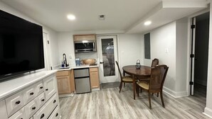 Una cocina compacta con microondas integrado, un televisor de pantalla plana grande y una zona de comedor con mesa y sillas de madera.