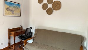 Et værelse med et træskrivebord, en sort kontorstol, en beige sofa og en vægdekoration i vævet materiale.