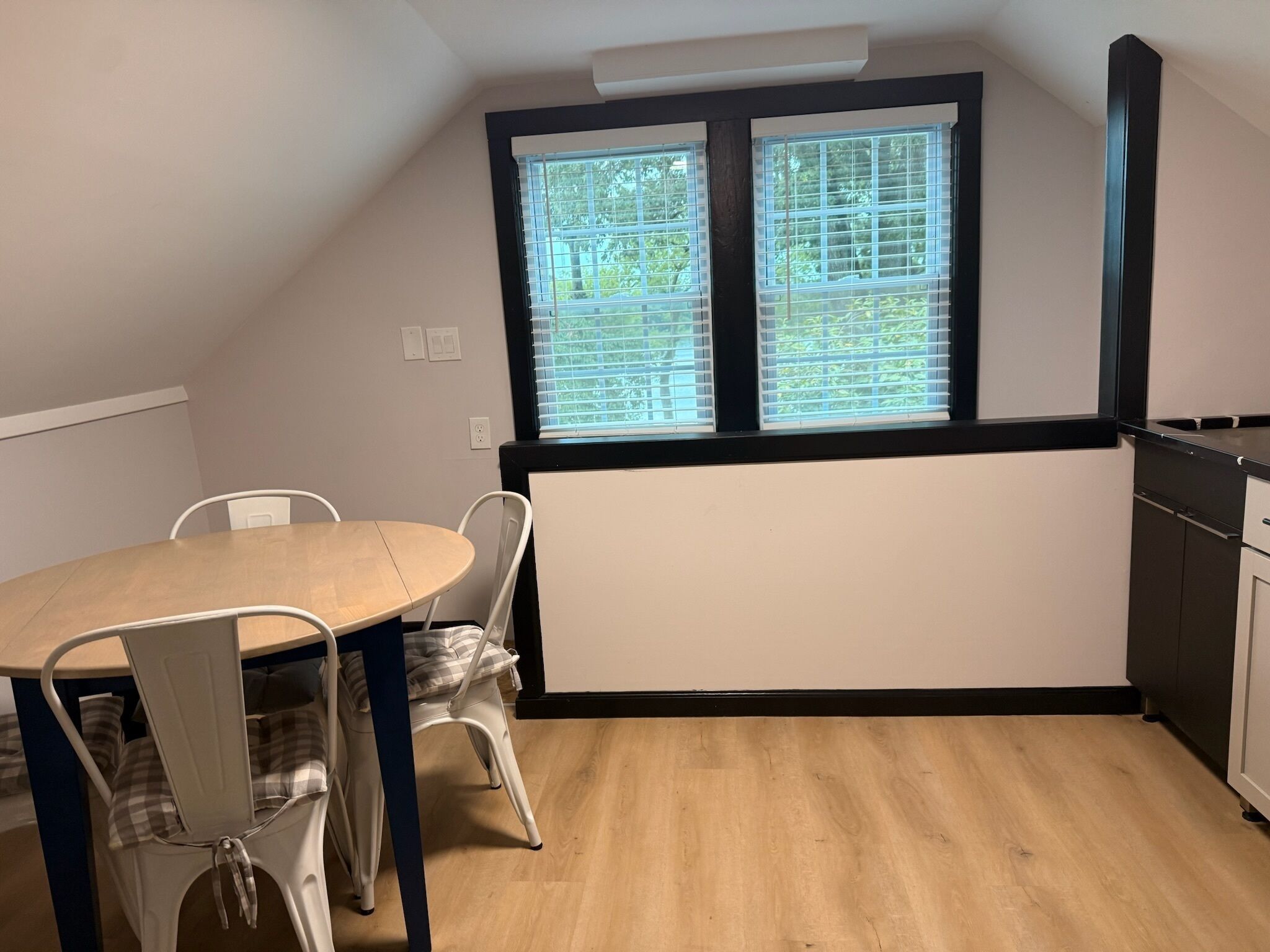 Um quarto com uma mesa de jantar, cadeiras, uma janela com persianas, um radiador e uma área de cozinha.