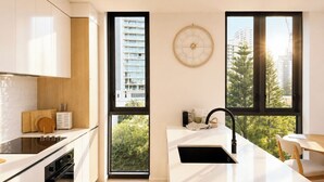 Una cocina moderna con una isla central, horno empotrado y un ventanal con vistas a edificios y árboles.
