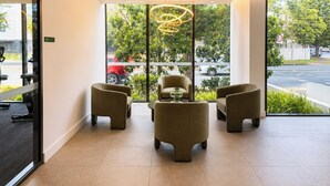 Un vestíbulo moderno con tres sillones, una lámpara circular singular y grandes ventanales con vista a la calle.