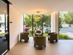 Eine moderne Lobby mit drei Sesseln, einer ungewöhnlichen runden Leuchte und großen Fenstern mit Blick auf die Straße.