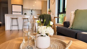 Una cocina moderna con armarios blancos, una zona de comedor con un sofá oscuro y una mesa con un posavasos tejido y un jarrón de flores blancas.