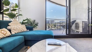 Un salon moderne avec un canapé bleu, une table basse et de grandes fenêtres donnant sur la ville.