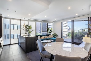 A modern apartment with a kitchen, dining area, and a balcony with a city view. - Elegant 3BR Retreat with Pool, Parking and Balcony (Phillip)