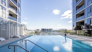 Une piscine à débordement située sur le toit, offrant une vue dégagée sur les gratte-ciel de la ville, et entourée de bâtiments modernes.