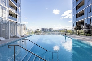 A rooftop infinity pool with a clear view of the city skyline, surrounded by modern buildings. - Elegant 3BR Retreat with Pool, Parking and Balcony (Phillip)