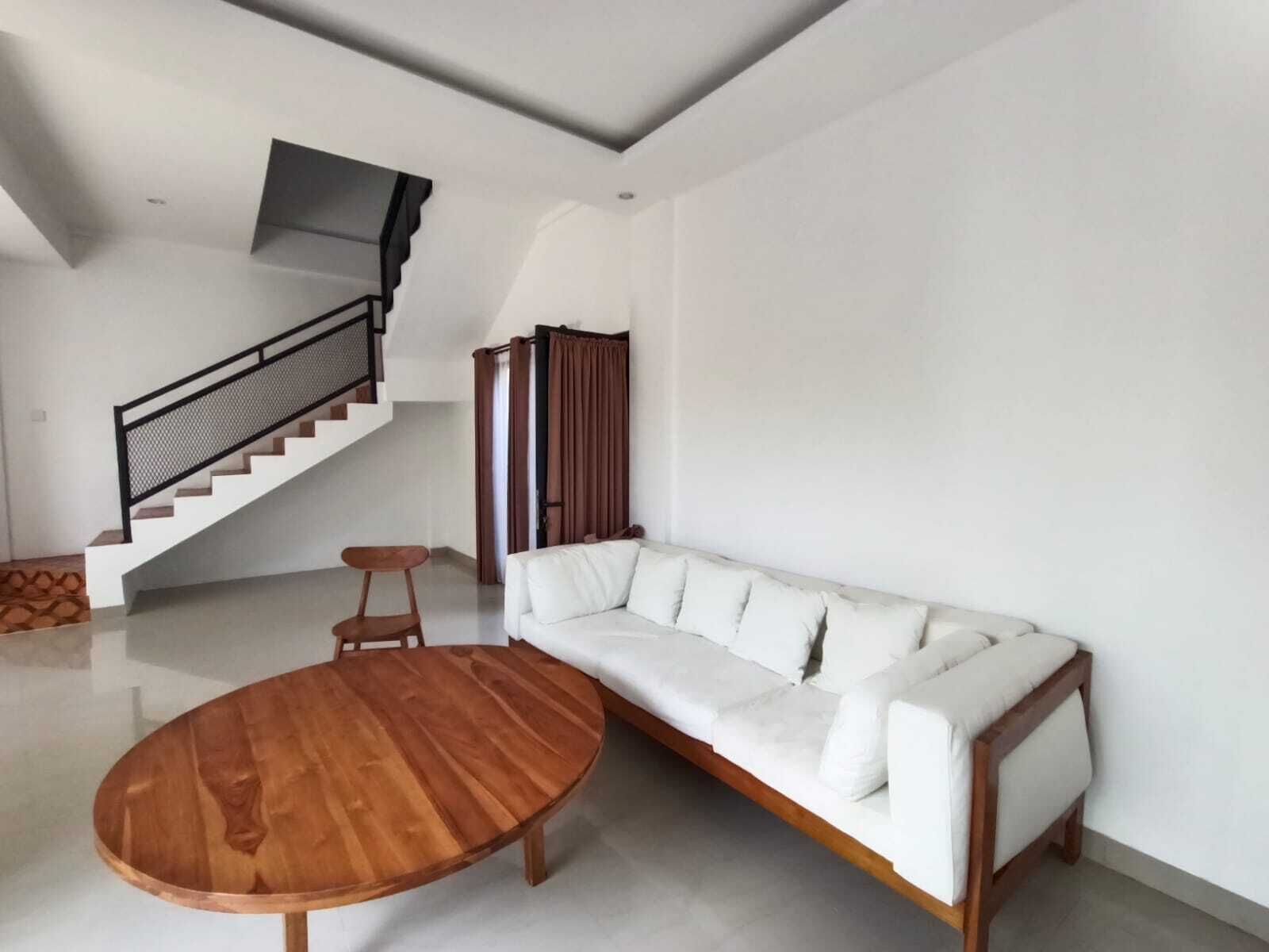 Un salón moderno con una mesa de centro de madera, un sofá blanco, una escalera y vistas al exterior.