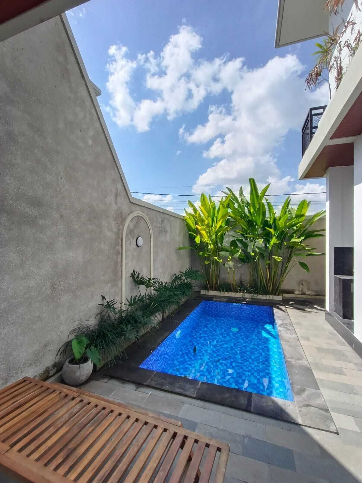A swimming pool with a tiled edge, surrounded by potted plants and a wooden bench.