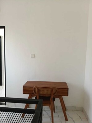 Ein Zimmer mit einem Holztisch, einem Korbstuhl und einem Bett mit schwarzem Rahmen.