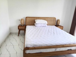 Ein Einzelbett mit Holzbettgestell und weißer Bettwäsche in einem Zimmer mit weißen Wänden und Fliesenboden.