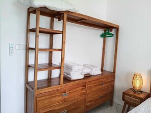 Een houten dressoir met laden en een plank, een groene kleerhanger en een brandende lamp op een nachtkastje.