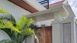 A building entrance with a wooden door, a potted plant, and a concrete wall. - Cozzy Villa Sakangi Mas (Tabanan)