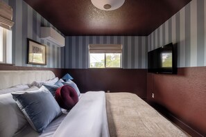Ein Hotelzimmer mit Bett, Fernseher, Fenster mit Jalousien und einer Klimaanlage.