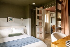 Ein Hotelzimmer mit einem Bett, einem Schreibtisch, einem Stuhl und einer Tür zu einem anderen Raum.