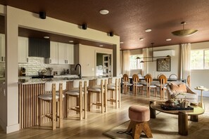 Una cucina moderna con isola centrale, sedie in legno e angolo pranzo con divano e tavolino.