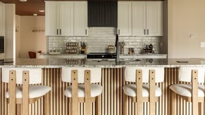 Una cocina moderna con gabinetes blancos, una isla central con taburetes de bar y una estufa integrada.