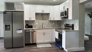 A modern kitchen with white cabinets, stainless steel appliances, and a marble backsplash. - vacation home close to the beach (Clearwater)