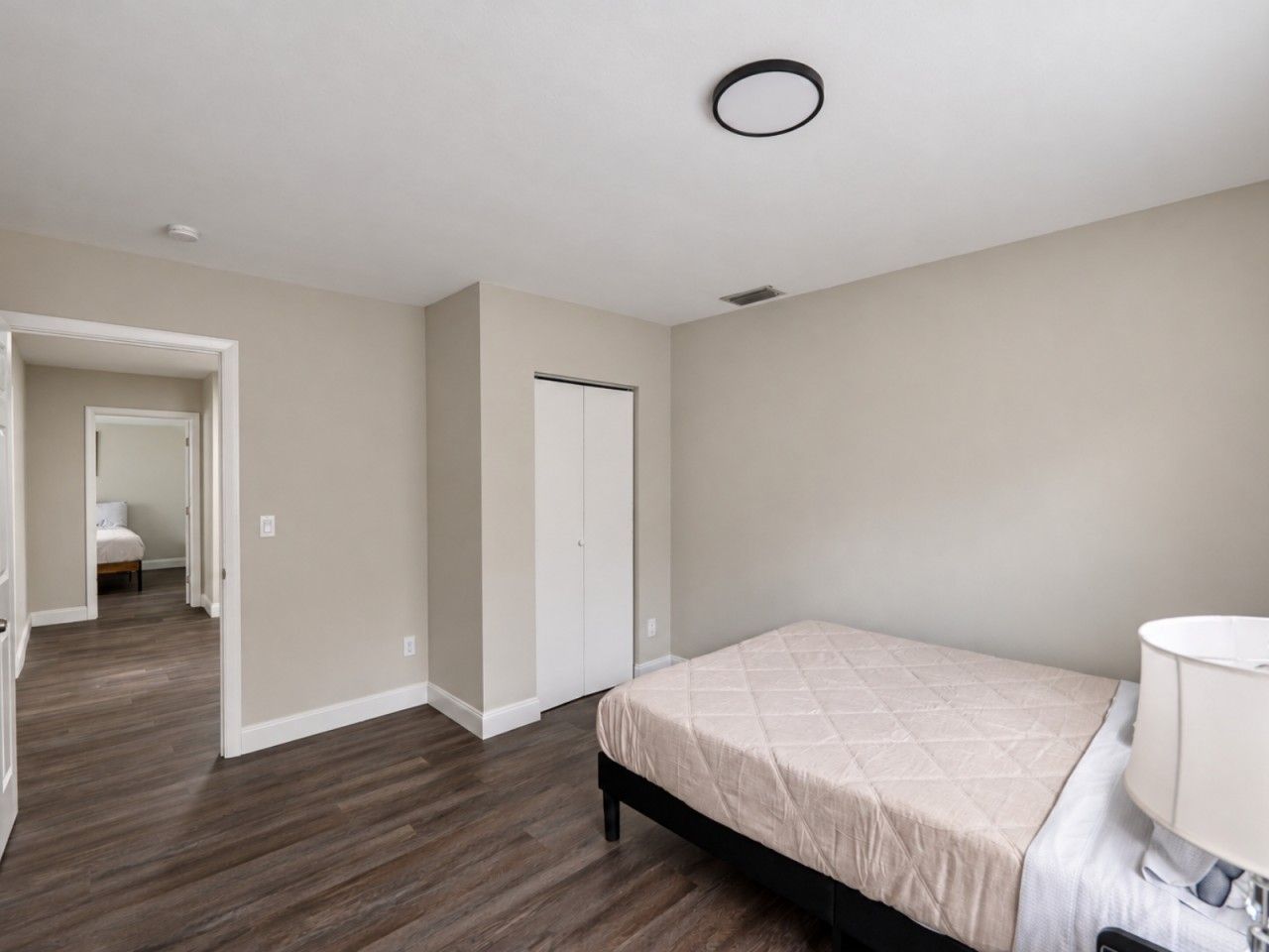 A bedroom with a bed, a bedside table, and a door leading to another room.