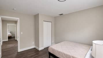 A bedroom with a bed, a bedside table, and a door leading to another room.