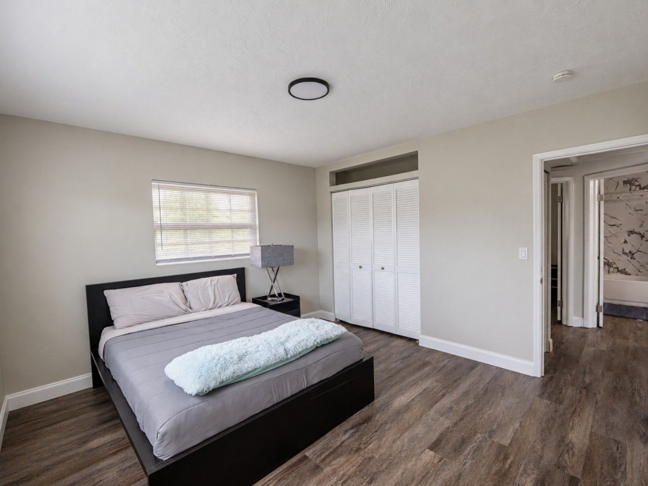 A bedroom with a bed, a nightstand, a window, and a closet.