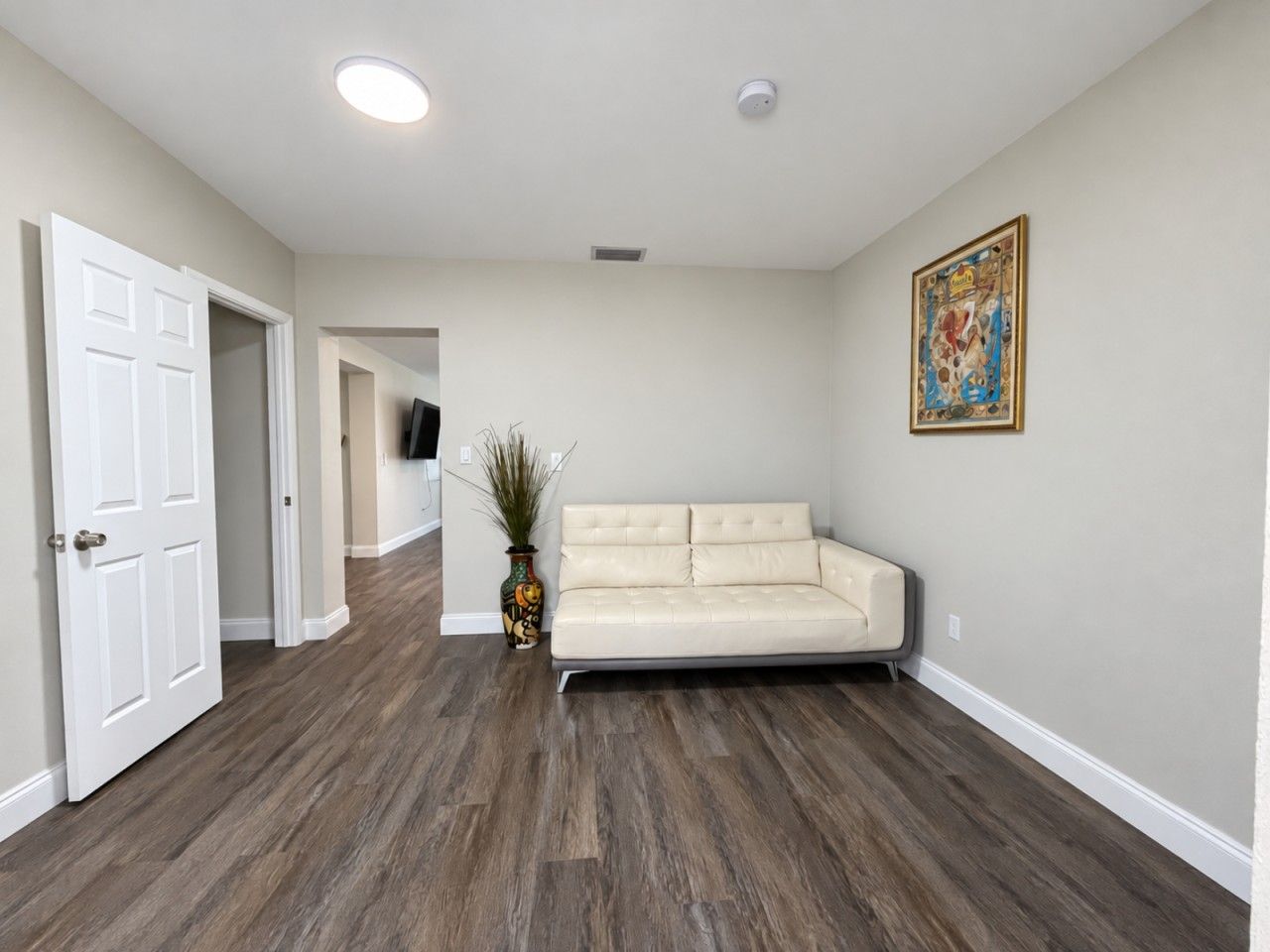 Une pièce avec un canapé beige, un téléviseur à écran plat fixé au mur et un plancher en bois.