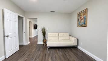 A room with a beige sofa, a flat-screen TV mounted on the wall, and a wooden floor.