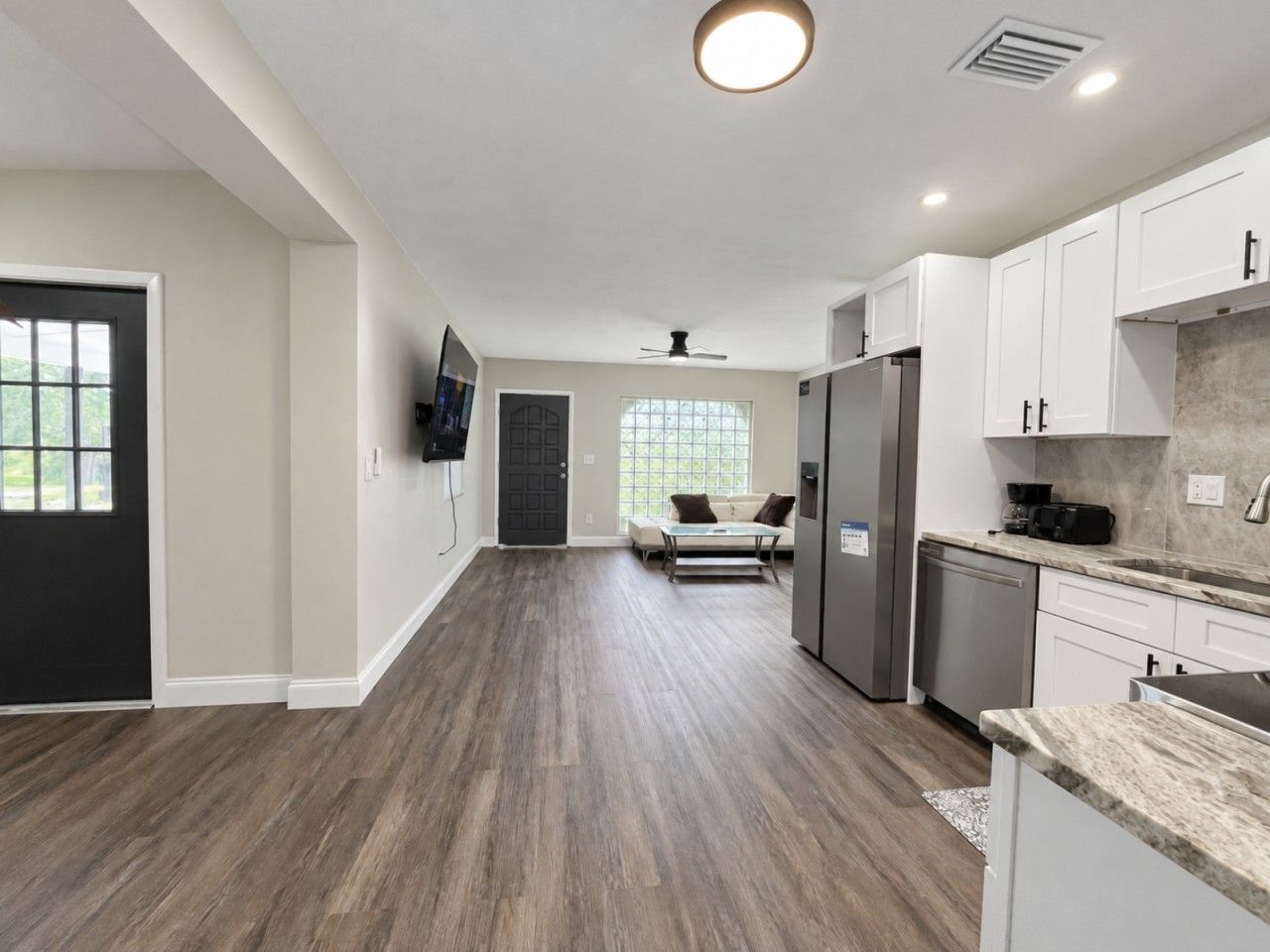 A modern kitchen with white cabinets, a stainless steel refrigerator, and a marble countertop.