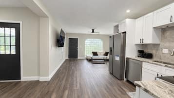 A modern kitchen with white cabinets, a stainless steel refrigerator, and a marble countertop.