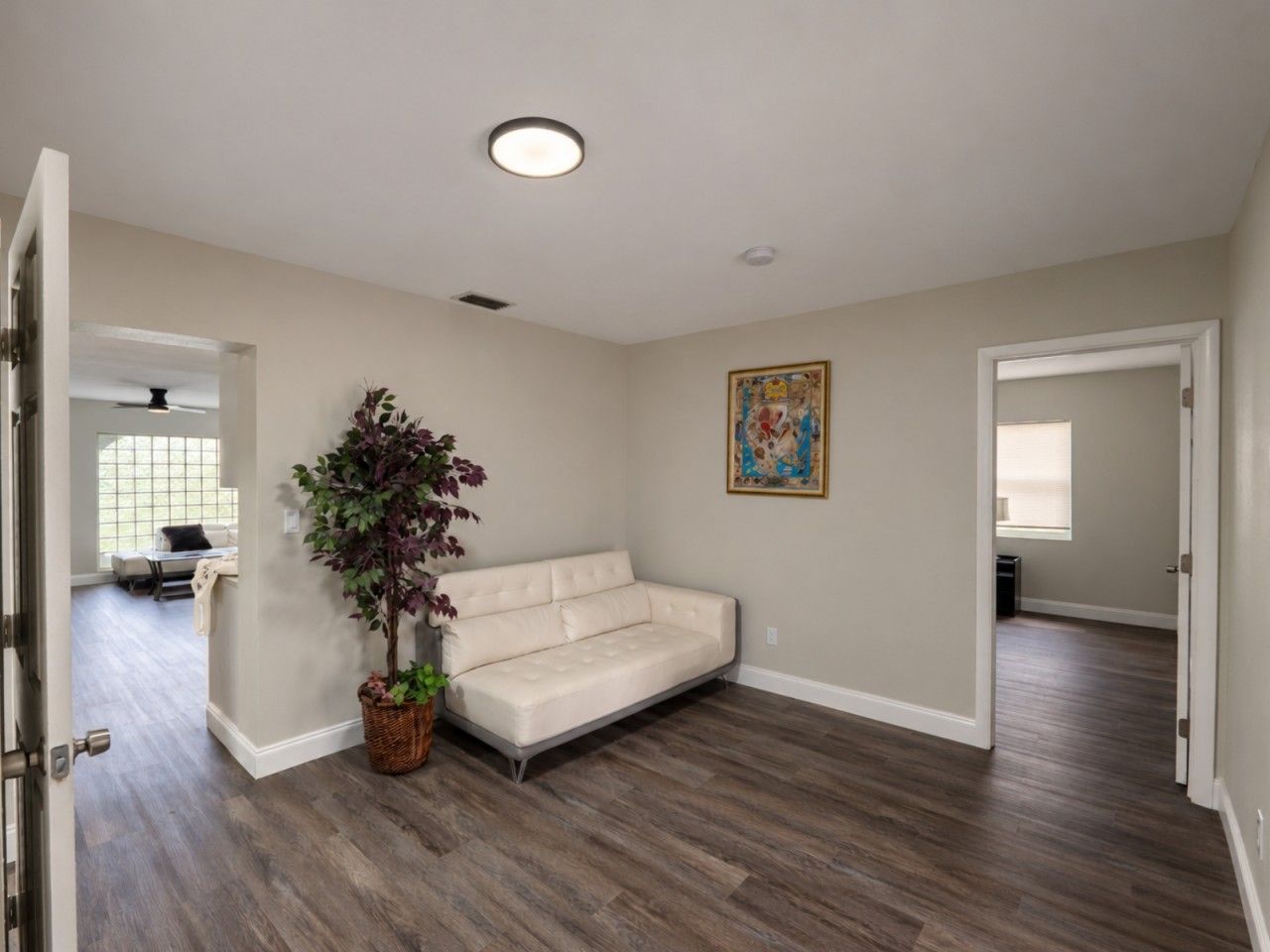 A room with a beige sofa, a potted plant, and a painting on the wall.