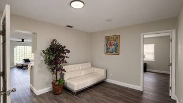 A room with a beige sofa, a potted plant, and a painting on the wall.